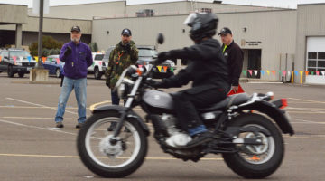 Motorcyclist riding in parking lot while instructors watch