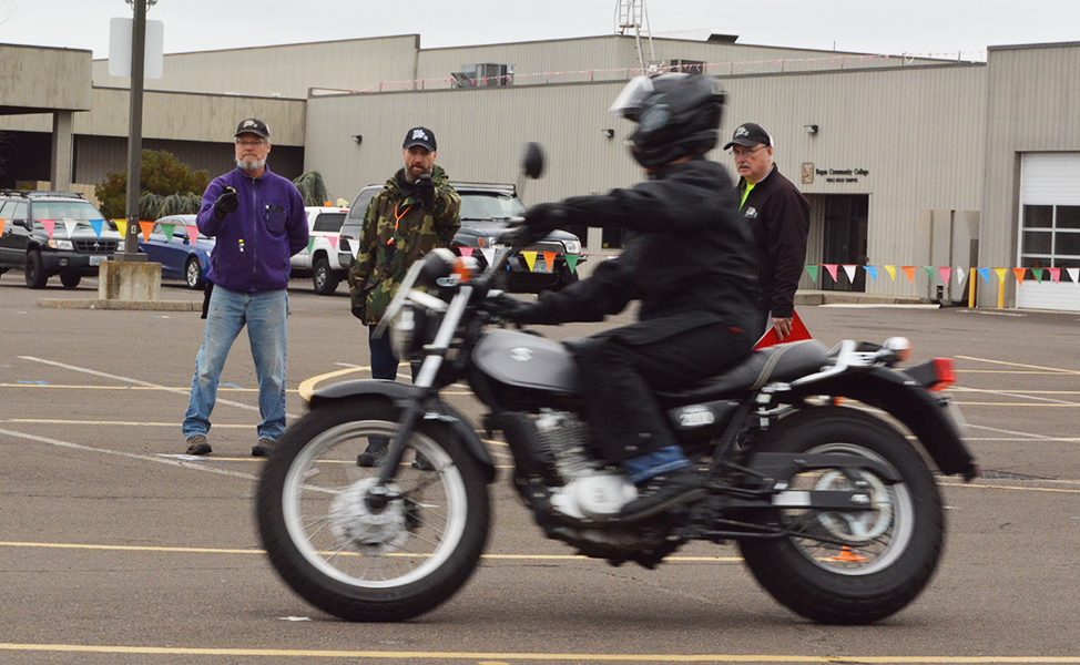 Motorcyclist riding in parking lot while instructors watch