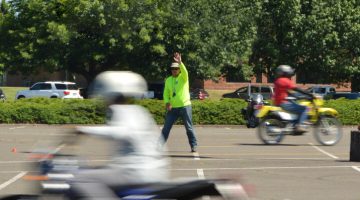 Instructor raising hand in parking lot while motorcycle students ride by.